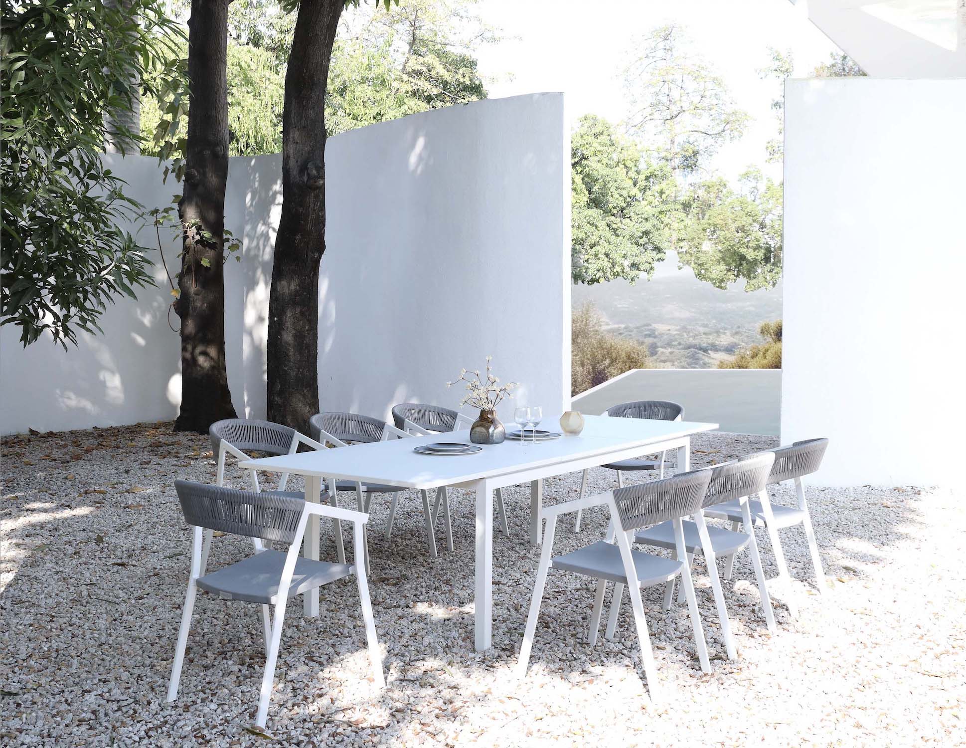 Table extensible en aluminium haut de gamme inoxydable blanc, design épuré méditerranéen, entourée de six chaises assorties.