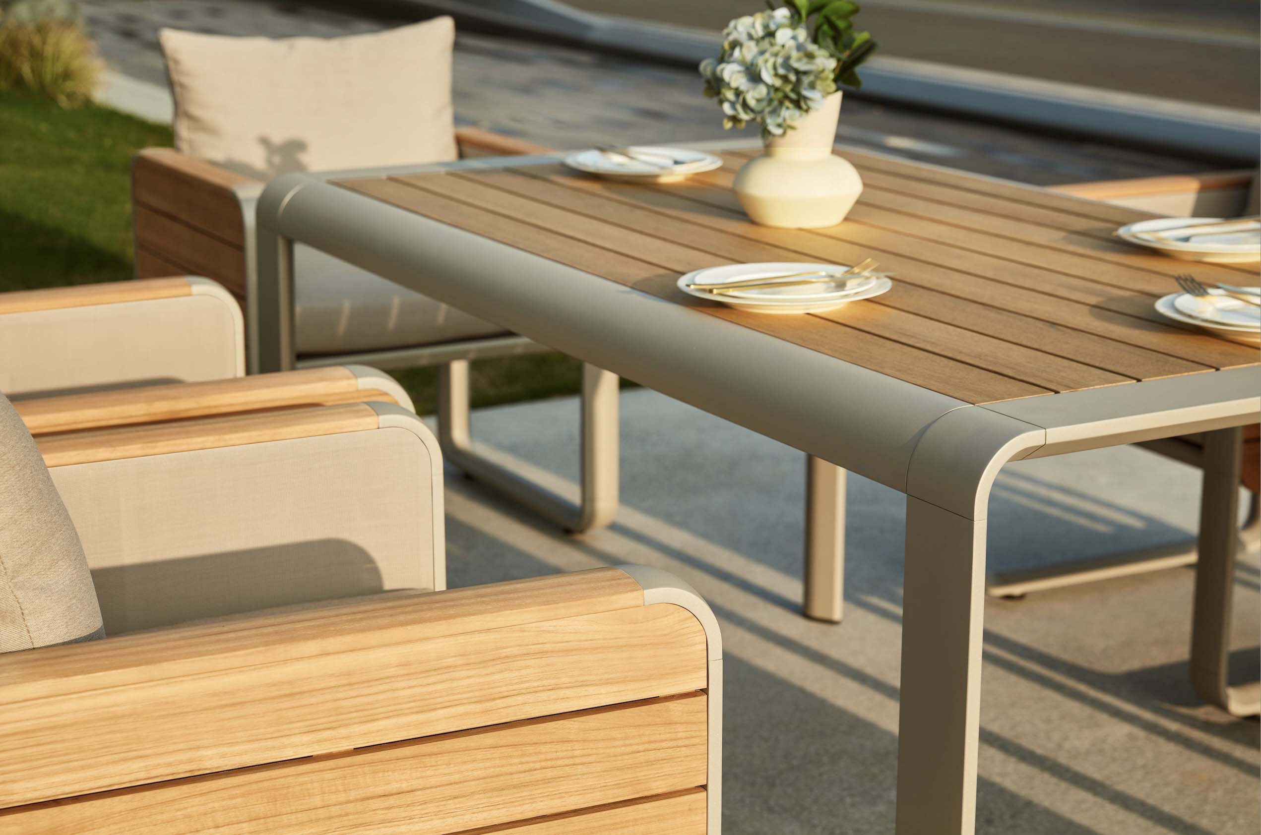 Ensemble repas extérieur haut de gamme en aluminium gris mat et plateau en teck FSC lisse avec courbes élégantes, coussins.