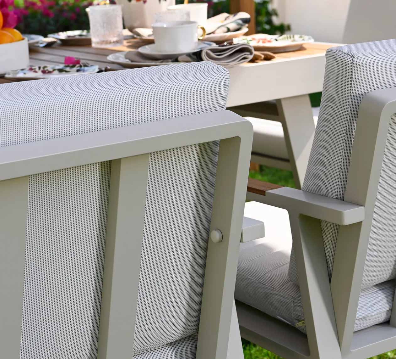 Détail d’un ensemble repas 4 places en aluminium haut de gamme et teck FSC, coussins en tissu oléfine beige avec housse.