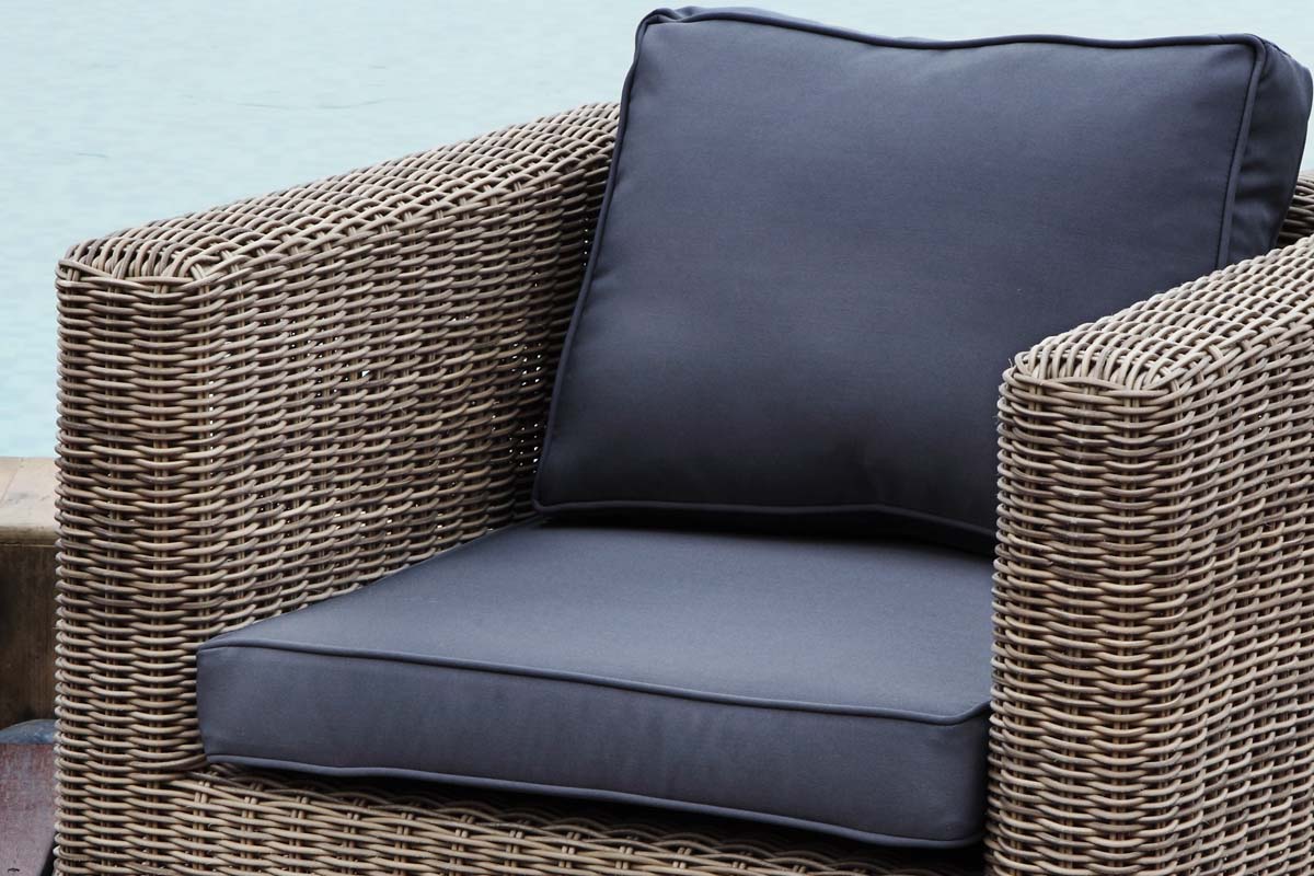 Fauteuil rustique en résine tressée ronde couleur osier avec coussins déhoussables gris foncé, tissu déperlant et structure.