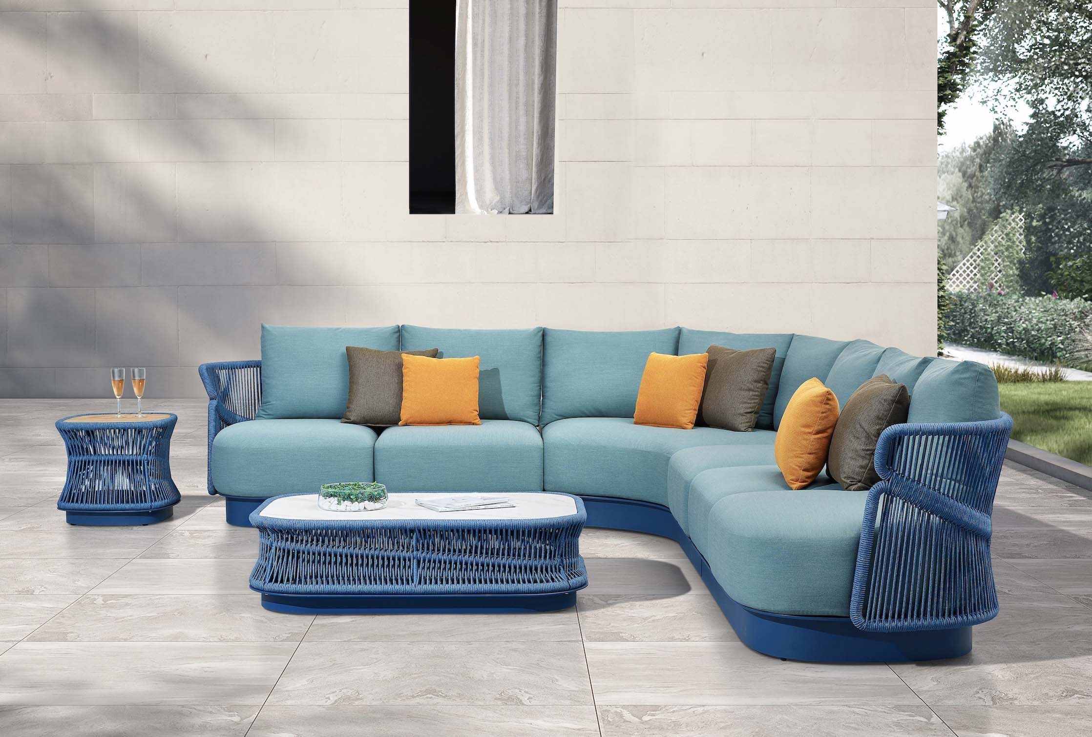 Salon d'angle de jardin luxueux en aluminium et corde tressée bleue, plateau céramique blanc, coussins bleu azur et orange. 