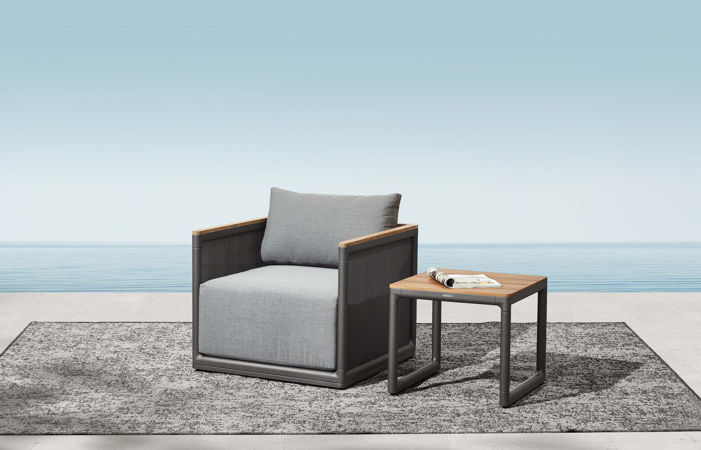 Fauteuil minimaliste en aluminium thermolaqué gris avec coussins en tissu Oléfine gris, accompagné d’une table basse carrée.