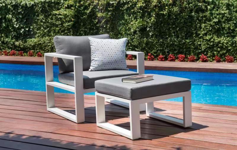 Fauteuil modulable en aluminium blanc haut de gamme avec coussins gris épais et repose-pied coordonné, design épuré. 