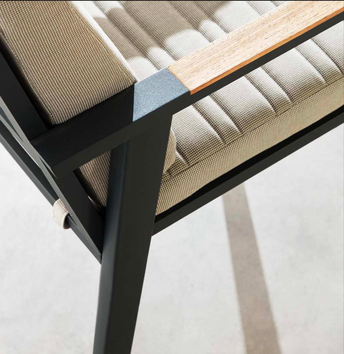 Détail d’une chaise avec structure en aluminium haut de gamme noir mat, accoudoir en teck FSC, coussin épais beige en tissu.