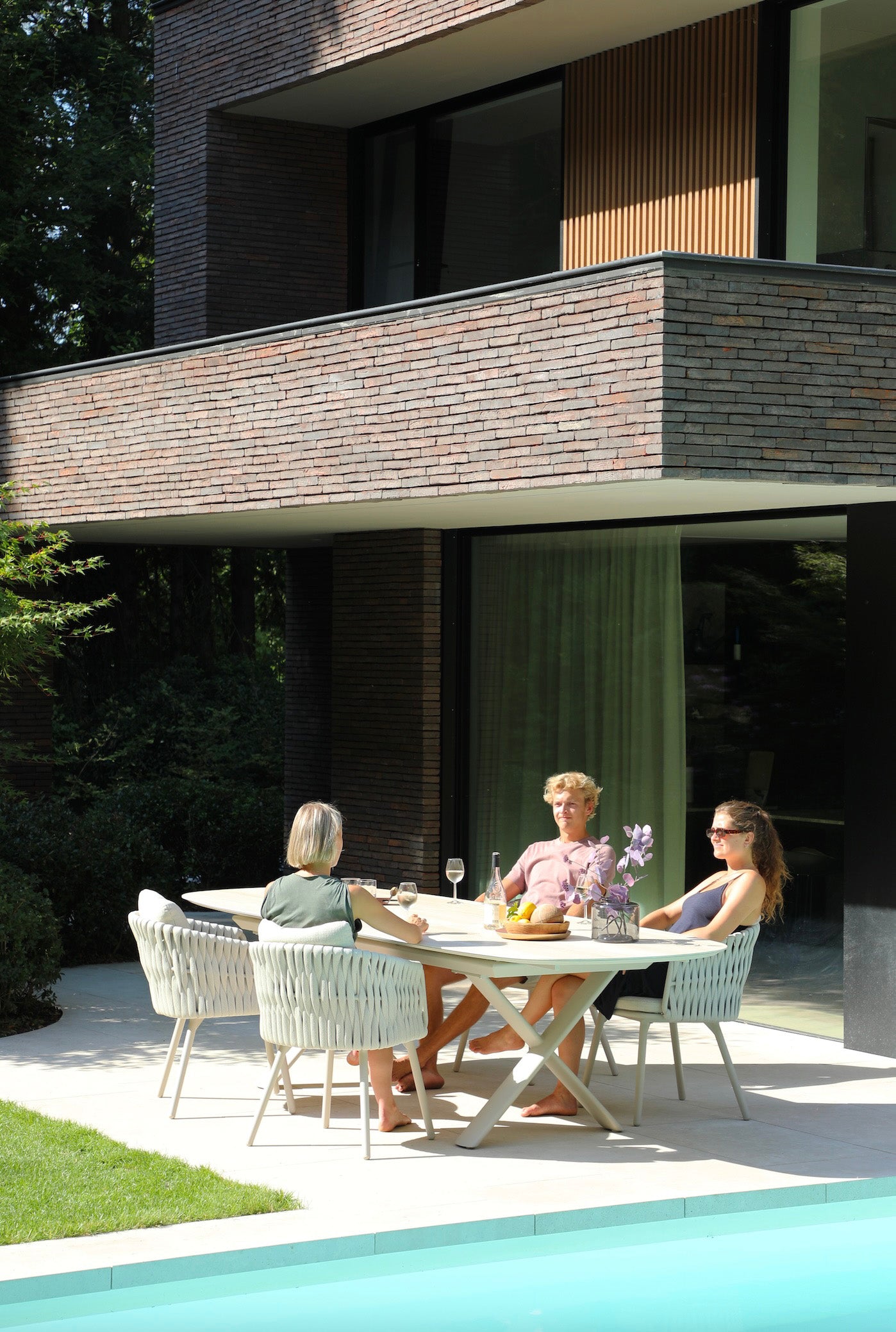 Fauteuils repas extérieurs en aluminium haut de gamme inoxydable et corde beige autour d’une table extensible au grand.