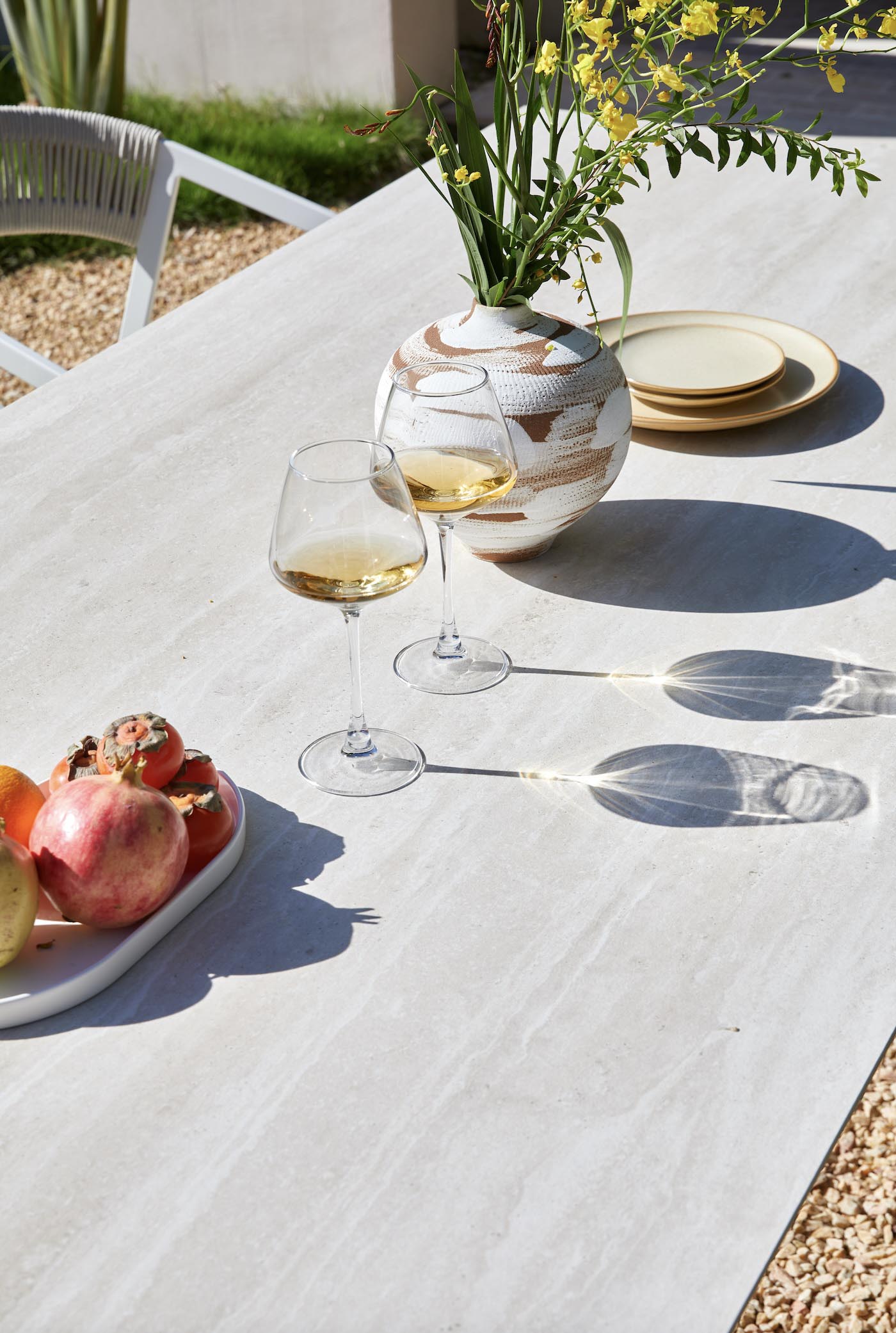 Table d'extérieur avec plateau en céramique blanc mat et structure en aluminium haut de gamme inoxydable, design épuré. 